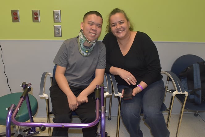 a teenager in a walker and neck brace smiling with an adult woman