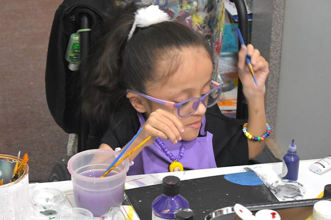 a child with glasses painting a picture with a paint brush