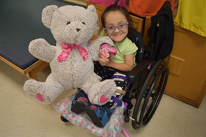 a child in a wheelchair holding a large teddy bear
