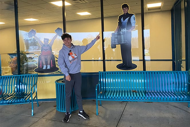 a teenager smiling an pointing at an image of him playing a marching snare drum
