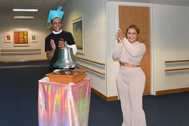Patient Leufry and his mom clapping and smiling near a metallic bell on a table
