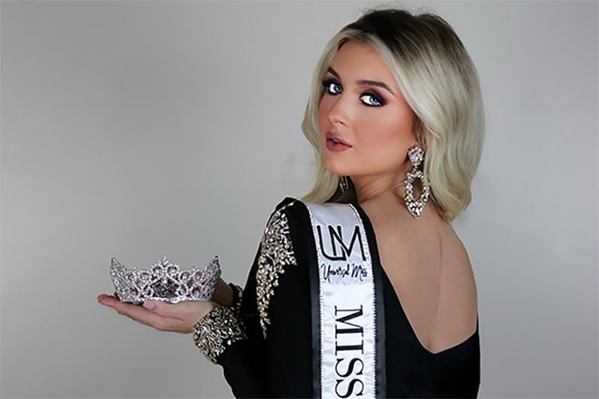 Patient Anna in a black pageant gown holding a tiara and wearing a sash that reads "Miss"