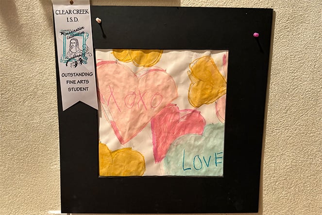 A painting featuring the words “XOXO” and “LOVE” inside two hearts. A white ribbon pinned to the top left corner reads “CLEAR CREEK I.S.D. OUTSTANDING FINE ARTS STUDENT”