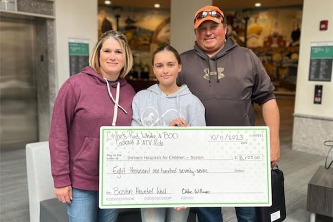 Patient with parents holding donation check for funds raised for Shriners Children's Boston