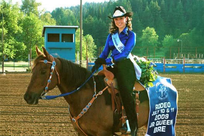 a child wearing a sash sitting on a horse with a cape that reads "Rodeo July 10 & 11 2009 Queen Bree"