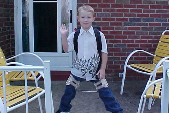 a child with leg braces wearing a backpack waving at the camera