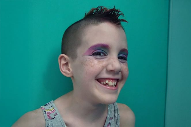 a smiling child with colorful makeup and a mohawk haircut