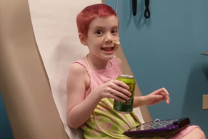a child with short, colorful hair holding a soda in an examination room