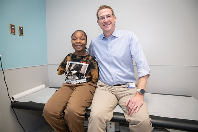 Patient Kaniyah and Joshua Pahys, M.D. smiling and sitting together on an examination table in his office