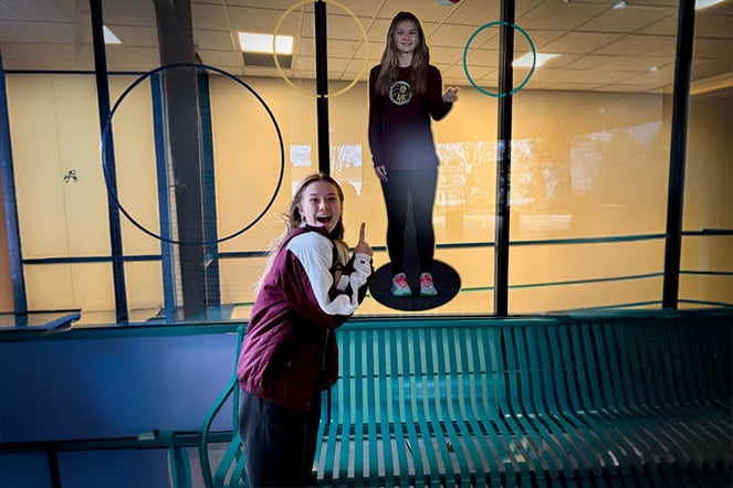 a teenager smiling and pointing at a window decal of an image of herself