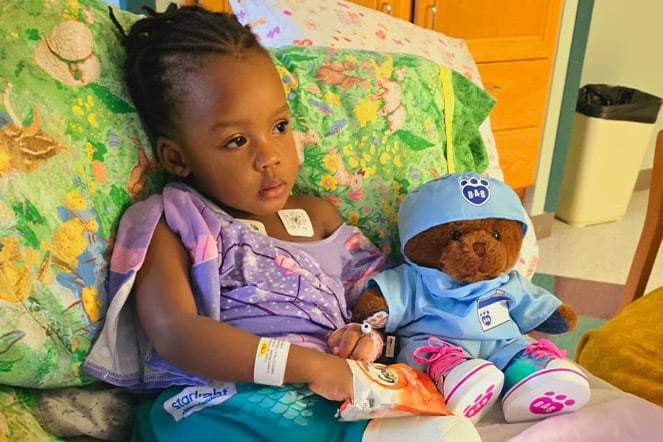 a child sitting in a hospital bed eating crackers with a teddy bear