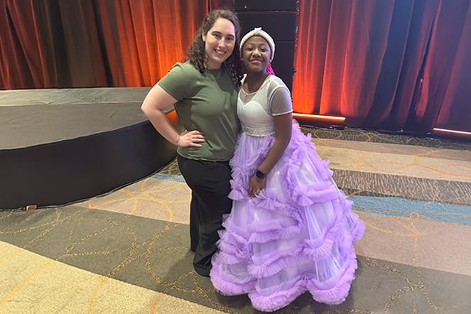 a woman and a teenager in a long colorful dress smiling together in a convention hall