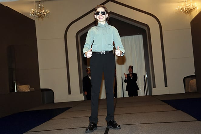 a teenage male wearing sunglasses giving two thumbs up on a fashion runway