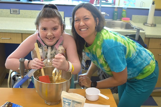 a young child and an adult woman mixing baking ingredients together in a large metal mixing bowl