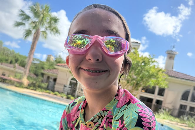 a smiling child wearing goggles by a pool