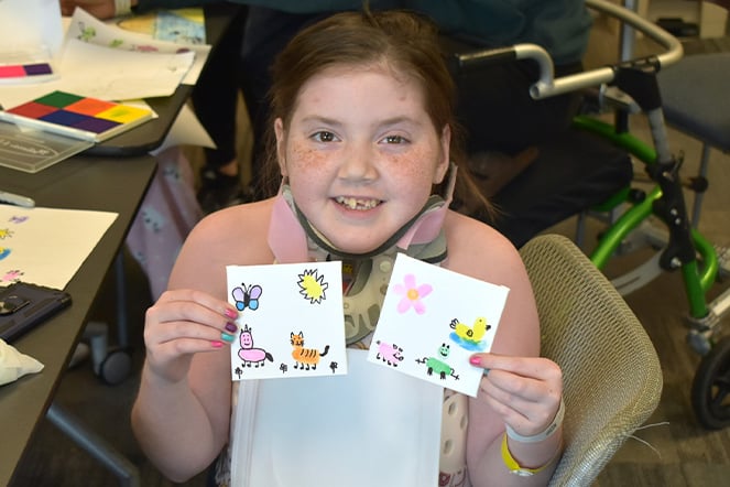 a child holding up two small paintings