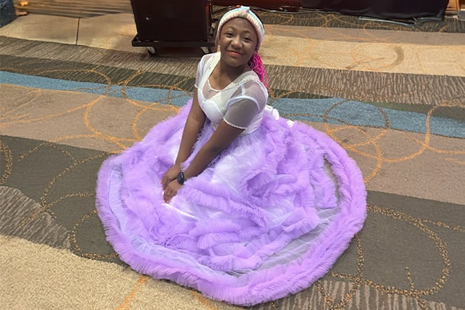 a child in a long, colorful gown sitting on the floor of a convention center