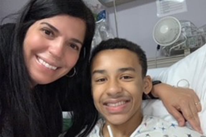 Shane smiling from hospital bed with mom leaning next to him