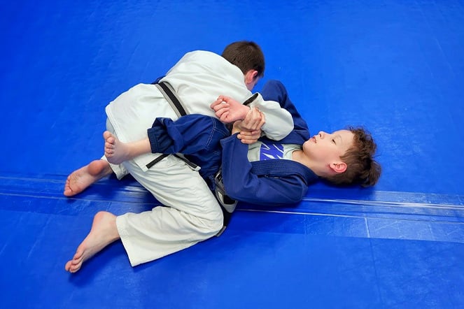 Spina bifida patient and his opponent engaging in ground combat while wearing traditional jiu jitsu kimonos
