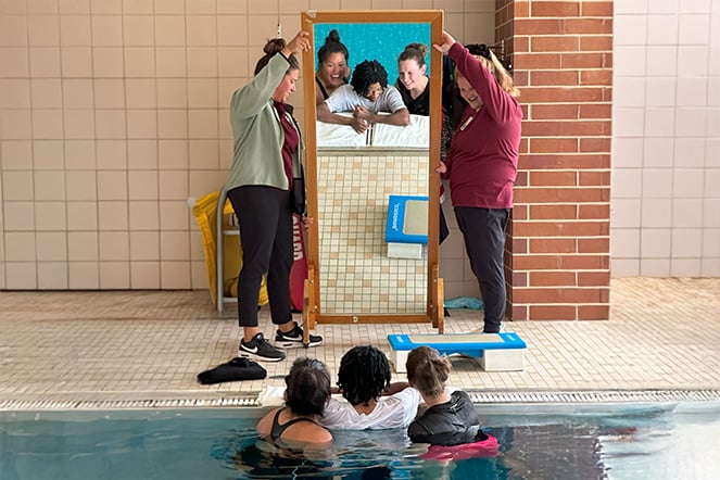 a teenager and two adults in a pool looking at themselves in a mirror that is being held up by two adults
