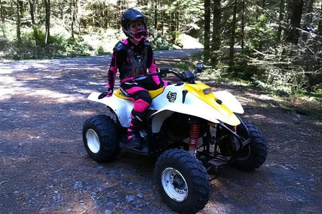 a child sitting on an all terrain vehicle in a forest