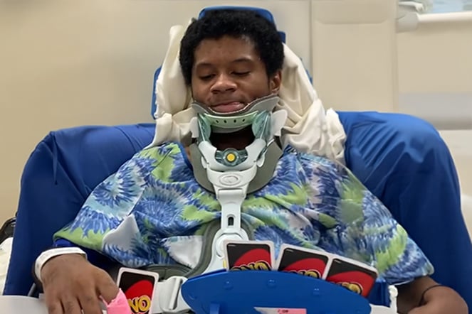 a child wearing a neck brace smiles in front of a had of Uno cards