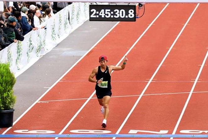  a runner crossing the finish line at a marathon race under a timer that reads "2:45:30:8."