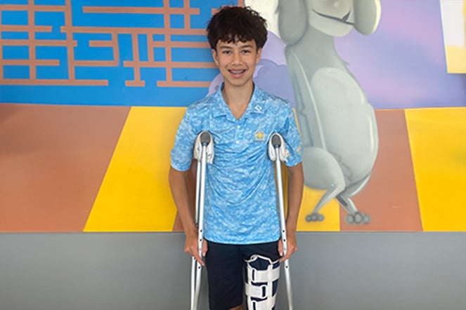 A smiling child with a leg brace and crutches standing in front of a mural