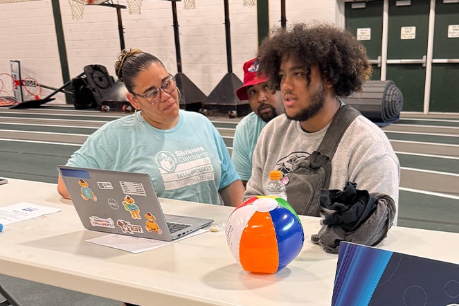 a teenager speaking with a person on a computer while two adults watch 