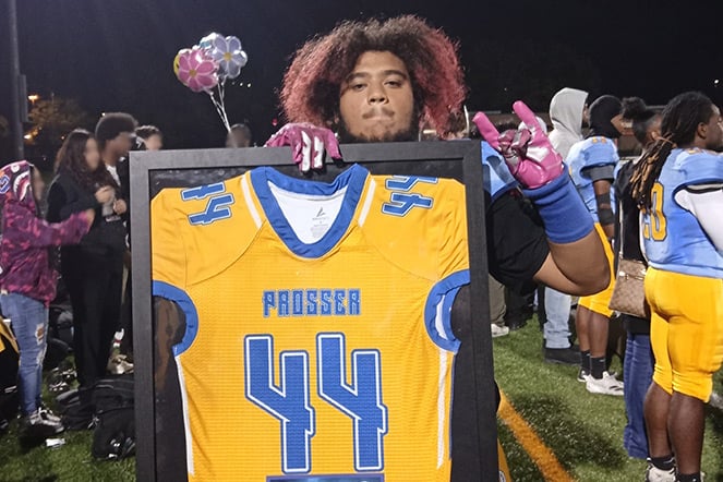 A teenage athlete holding up a framed football jersey that reads "Prosser" and the number 44