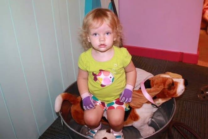 Toddler burn patient wearing protective gloves sitting with a dog plushie