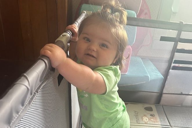 an infant standing and holding herself up against a gate