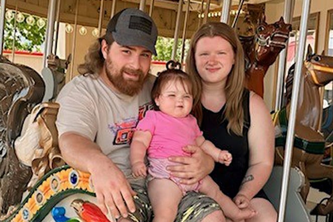 two adults holding an infant on a carousel 