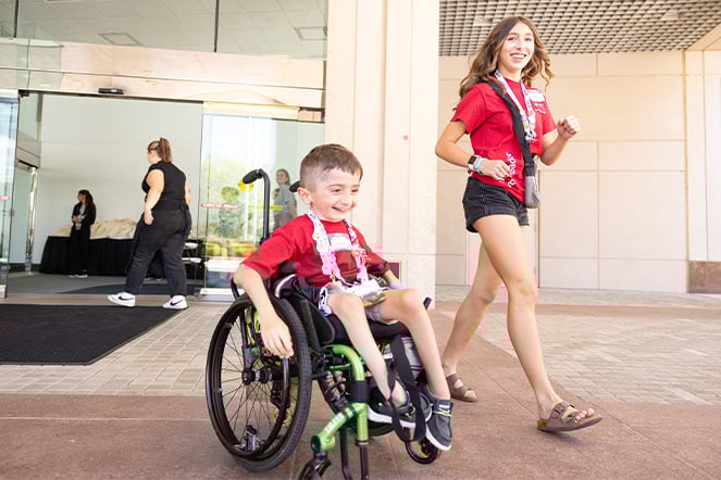 a child in a wheelchair and a teenager happily exiting a building in the same direction