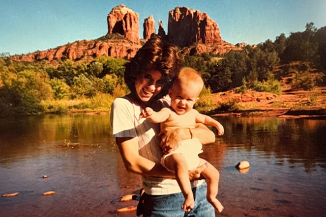 a vintage photo of a woman holding an infant in front of a mountain range