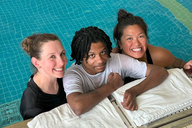 a child smiling in between two adults at the edge of a pool