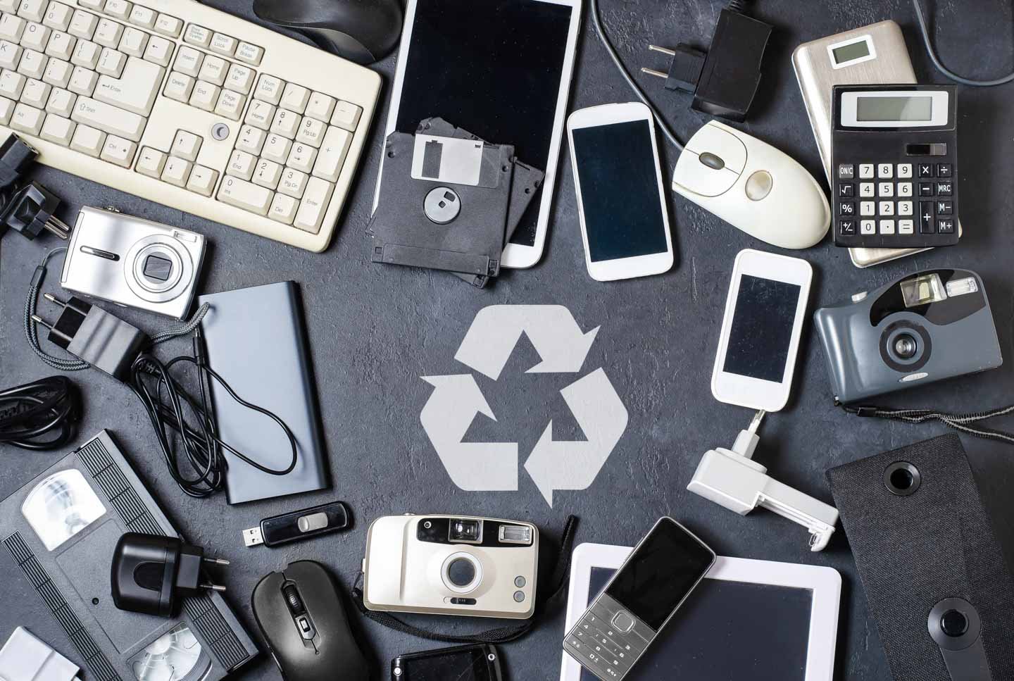 electronic tech scattered on table with recycle icon in the middle