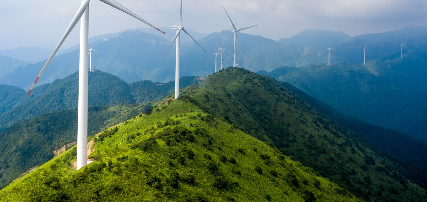 wind turbines on a grassy hill with blue mountains in the background