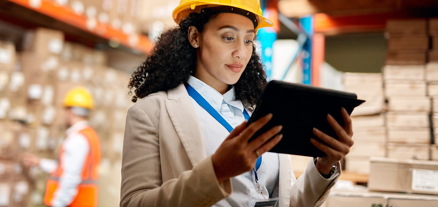 woman in hardhat in warehouse looking a tablet