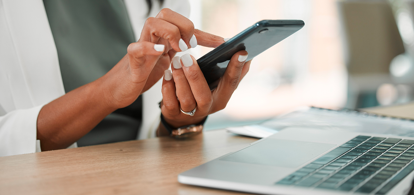 hand typing on phone, computer in the corner