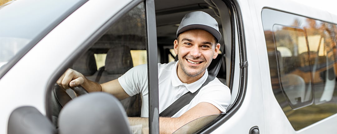 Person in a white van leaning out the open driver-side window on a sunny day.