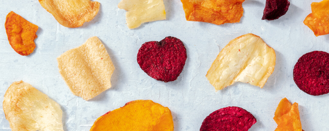 Colorful assorted vegetable chips, including a heart-shaped red chip, scattered on a light surface.