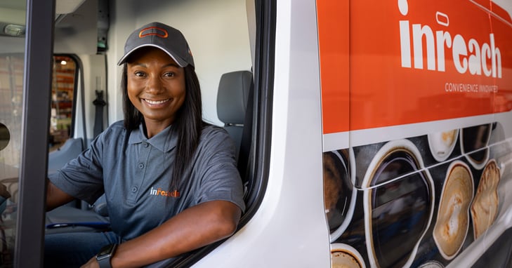 Person sitting in an inReach-branded delivery van wearing a uniform and cap.