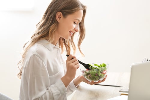 A woman eating a salad in front of a laptop.