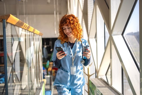 A healthcare worker walking and scrolling on her phone.