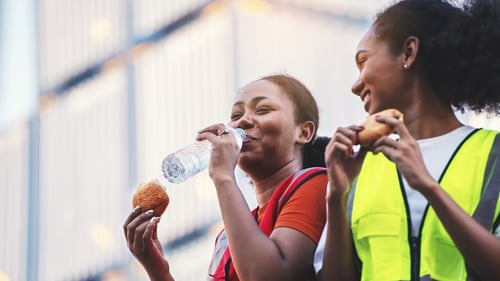 Two women on a remote energy worksite drinking water and eating during a work break.