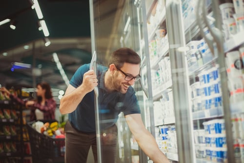 A man reaching for a drink in a freezer aisle of a supermarket.