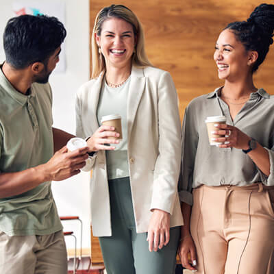 Group of coworkers standing together and talking while holding coffee cups.