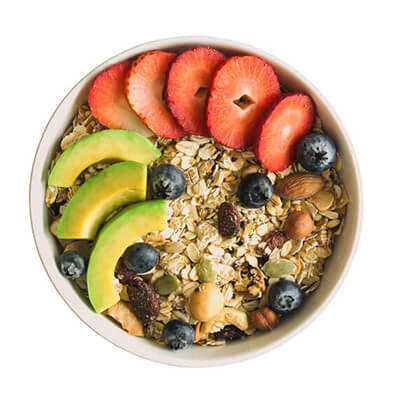 Bowl of oatmeal topped with sliced strawberries, avocado, blueberries, nuts, and seeds for a healthy breakfast.