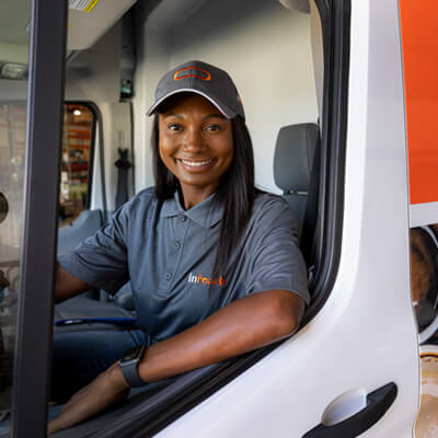 Person sitting in an inReach-branded delivery van wearing a uniform and cap.